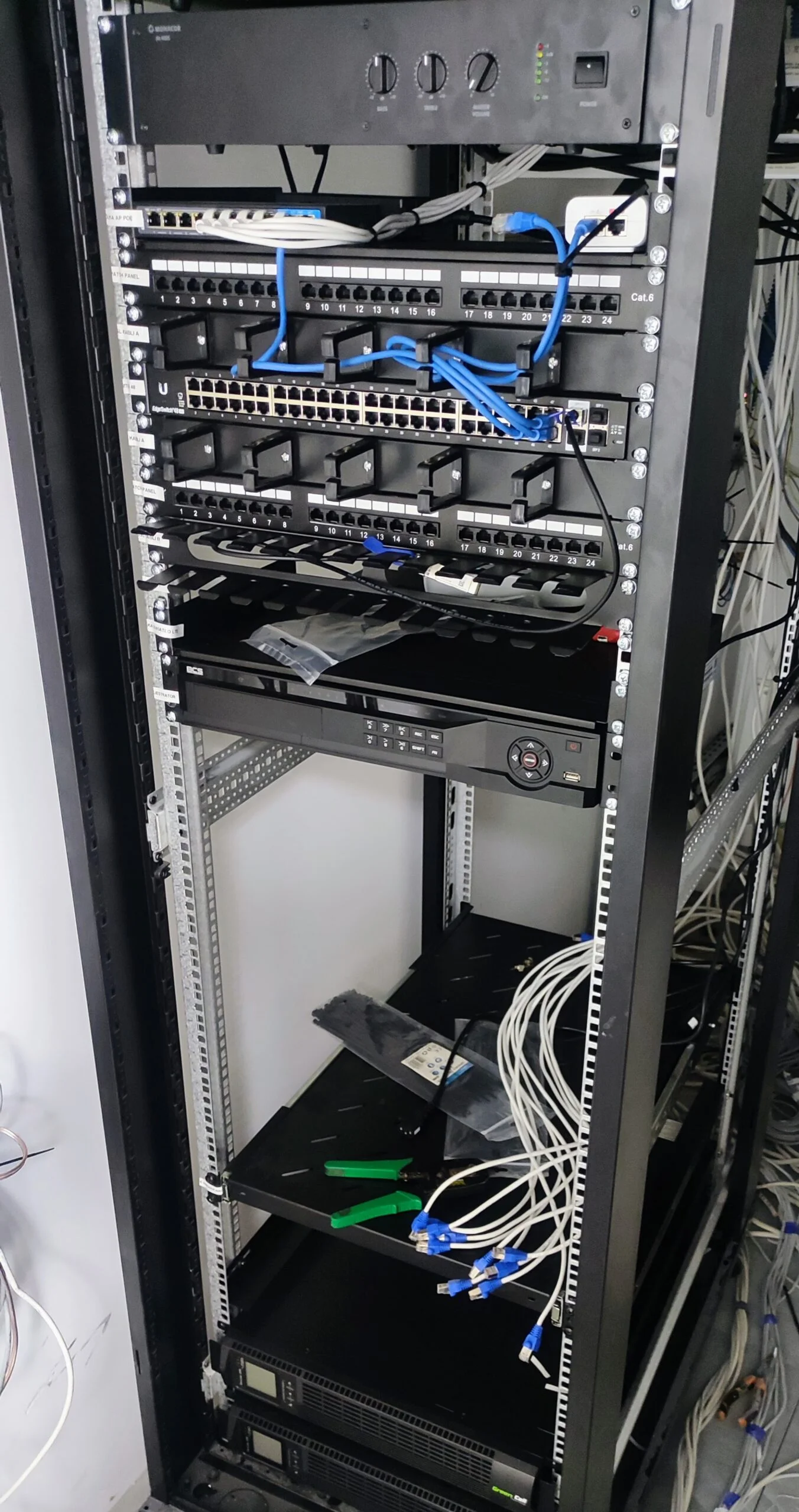 Szafa serwerowa z zainstalowanym sprzętem sieciowym i okablowaniem, przedstawiająca zaawansowaną infrastrukturę IT w trakcie instalacji lub konserwacji.