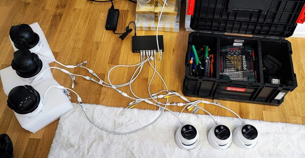 Sprzęt monitoringu wizyjnego rozłożony na podłodze, przygotowany do instalacji, z widocznymi kamerami, przewodami i skrzynką narzędziową.